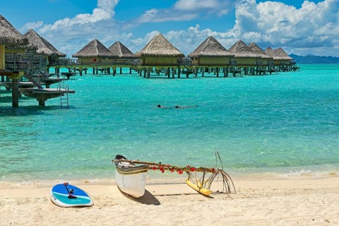 Decorated outrigger boat in front of overwater bungalows