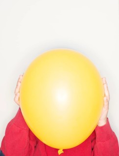 Child holding a yellow balloon in front of face