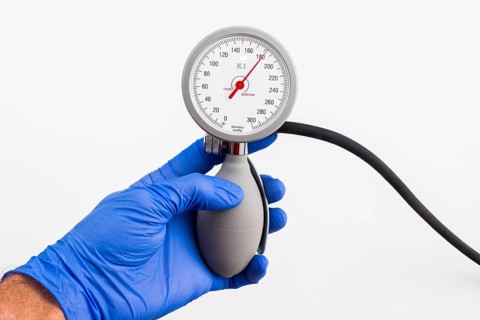A hand with a blue medical glove is holding a sphygmomanometer