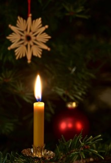 Burning candle in front of a Christmas tree with a star made of straw and a Christmas bauble