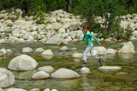 Girl jumping over rocks in the river Solenzara