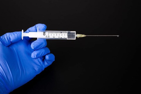 A hand with a blue medical glove is holding a syringe