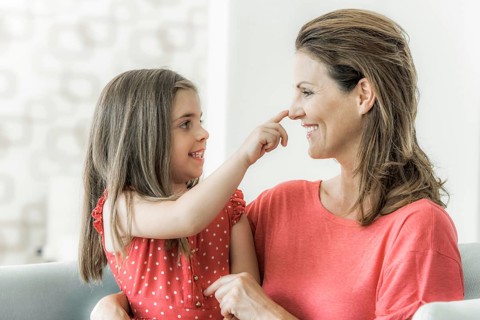 Mother and daughter sit on the couch together and look at each other
