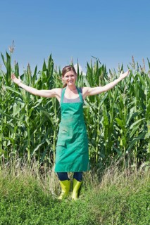 Young woman in work clothes standing with outstretched arms in front of a maize field