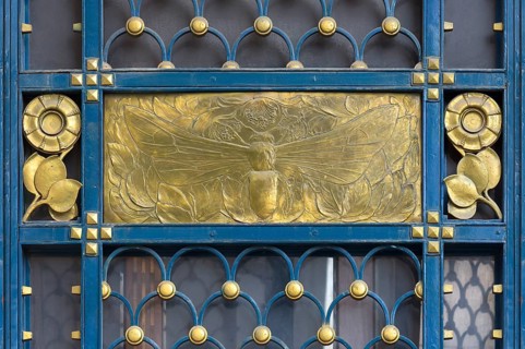 Gold-coloured relief of a bee at a wrought-iron gate around 1900