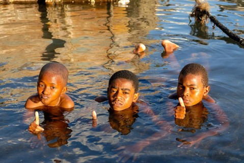 Three boys in the water showing a thumbs up