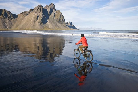 Woman riding a bicycle on the beach in front of Mt Vestrahorn near Hoefn
