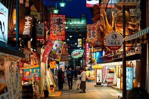 Many colorful neon signs in a pedestrian zone with shops and restaurants