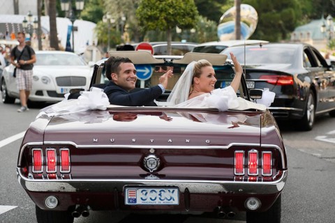 Bride and groom riding in an open Ford Mustang convertible car through the city