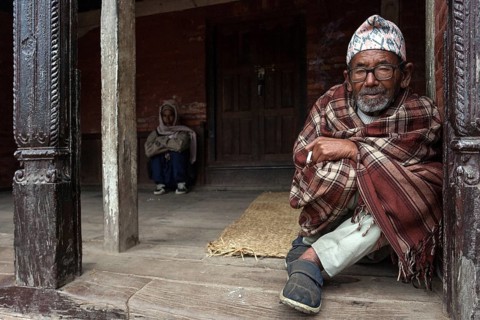 Nepalese man wrapped in a blanket sitting at an entrance