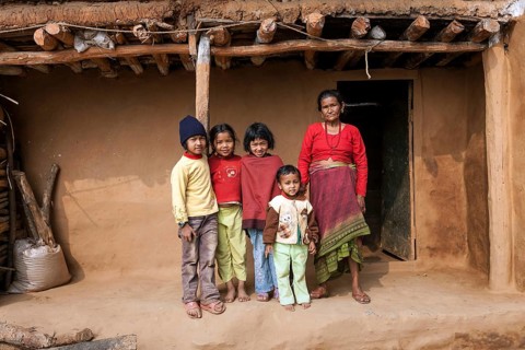 Old Nepalese woman and four children in front of a typical Nepalese rural house