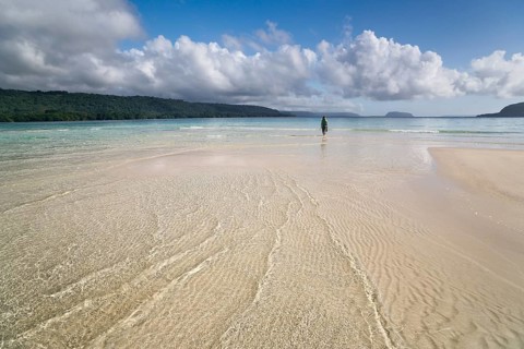 Woman walking across a sandbank to the beach