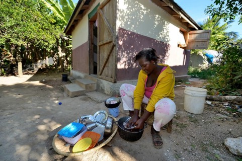 Young woman washing the laundry in front of the house which was given to the family by a relief organisation
