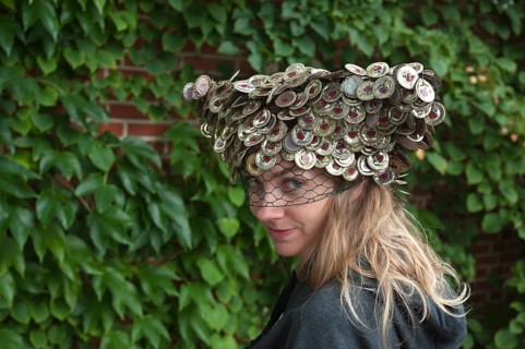 Young woman wearing a hat made of crown corks in front of a wall of leaves