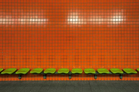 Green seats in front of an orange tiled wall in an underdground station
