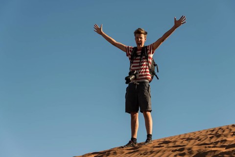 Teenager with photo camera standing on a dune and spreading his arms