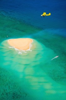 Small plane flying over coral reef with sand island