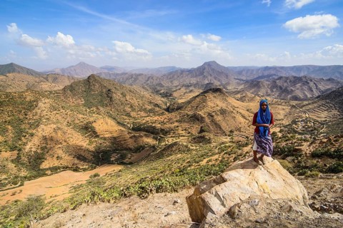 Local woman standing on a rock in front of the mountain scenery along the road from Massawa to Asmarra