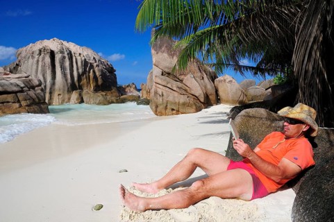 Tourist wearing a hat and reading book on Anse Patates beach