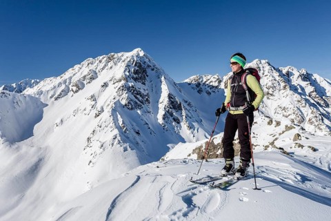 Ski tourer on the summit of Mt Seespitz in the Deutschnonsberg area with the mountains Illmenspitz and Proves at the back