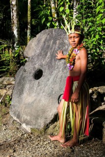 Traditionally dressed boy standing in front of stone money