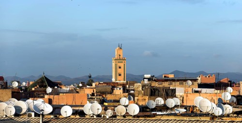 View across the roofs with satellite dishes to a minaret and the Atlas Mountains