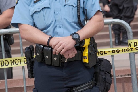 Policeman carries a gun on his right and a taser on his left