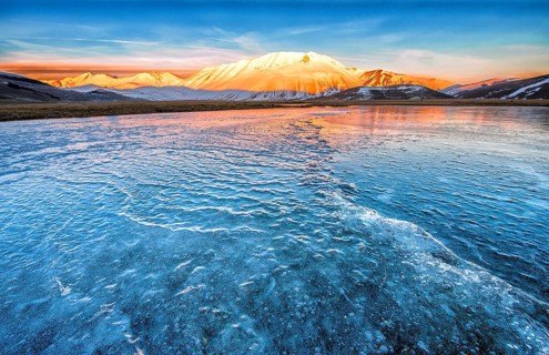 Monte Vettore in the evening light with a frozen puddle with small waves