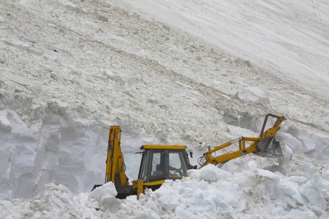Excavator shovelling away the snow of an avalanche