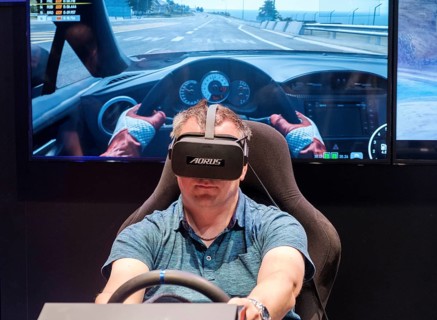Visitor wears Virtual Reality glasses in a driving simulator for car racing at gamescom