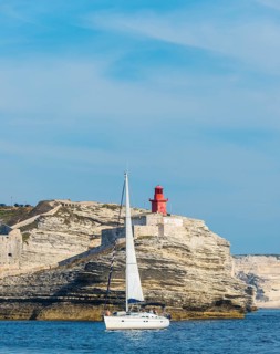 Sailing boat off the chalk cliffs and the lighthouse of Bonifacio