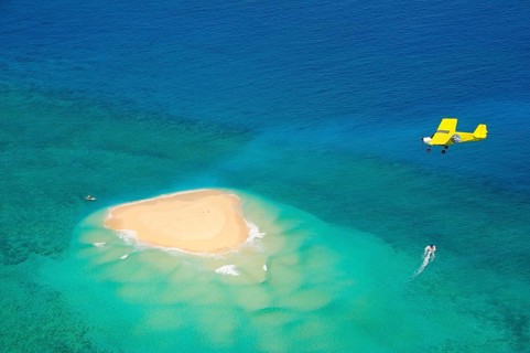 Small plane flying over coral reef with sand island