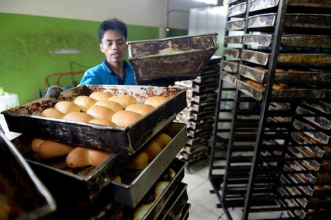Young man in a bakery taking bread out of the oven
