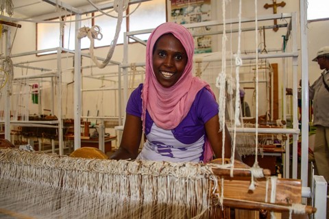 Friendly woman working on a hand weaving loom in a social project