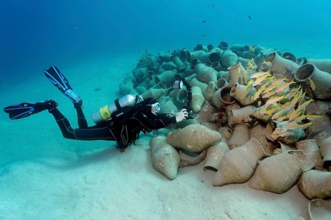 Underwater photographer photographing school of fish on amphora