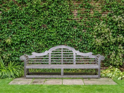 Wooden bench designed by Sir Edwin Lutyens in the rose garden at Sissinghurst Castle with Clematis 'Perle d'Azur' at back