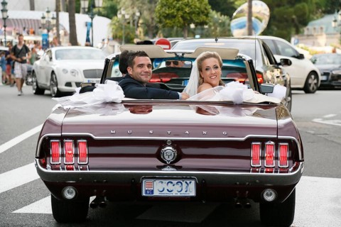 Bride and groom riding in an open Ford Mustang convertible car through the city