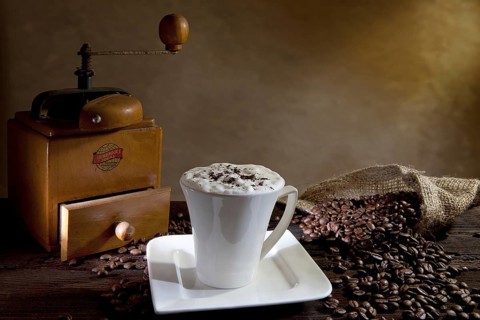 Cup of cappuccino with coffee beans and an old coffee grinder