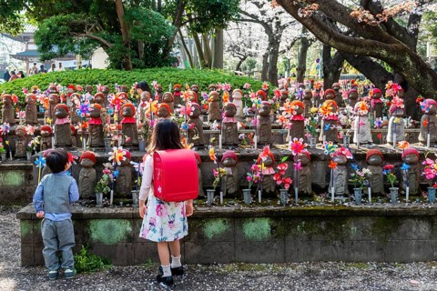 Two schoolchildren in front of Jizo statues with red caps