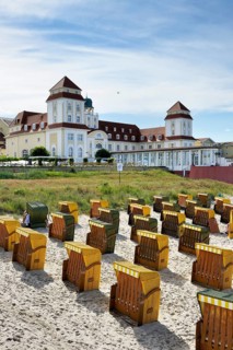Roofed wicker beach chairs on the beach in front of the Kurhaus spa building