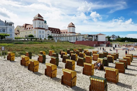 Roofed wicker beach chairs on the beach in front of the Kurhaus spa building