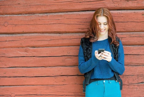 Young woman with red hair smiling and looking at her mobile phone
