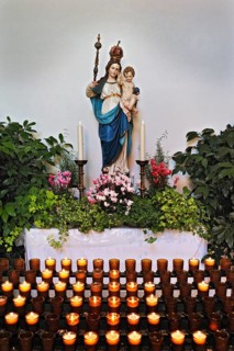 Sacrificial candles and a statue of Mary wearing a crown holding baby Jesus