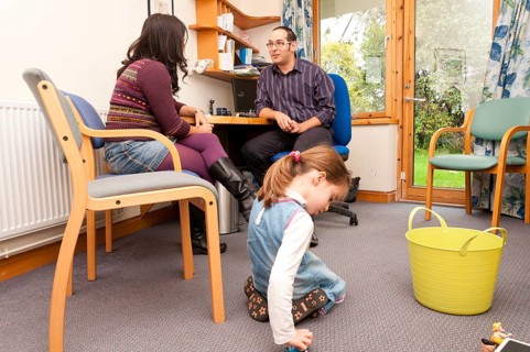 Child playing with toys while her mother talks to a GP doctor