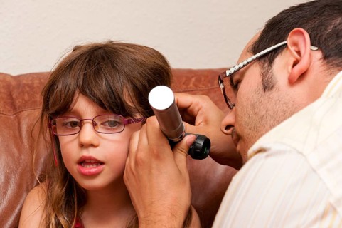 Doctor during a home visit examining a girl with an otoscope