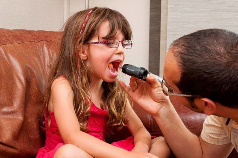Doctor during a home visit examining a girl with an otoscope