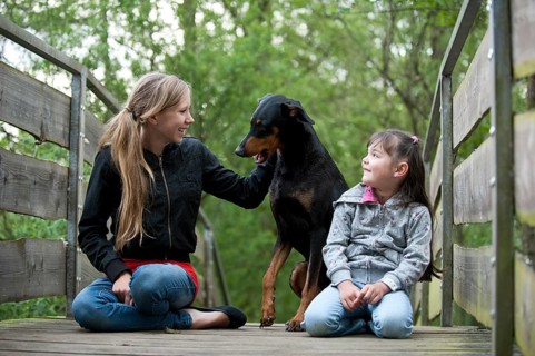 Two girls sitting with a Doberman on a bridge