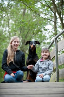 Two girls sitting with a Doberman on a bridge