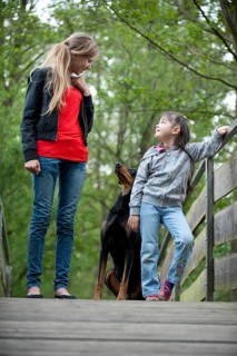 Two girls standing with a Doberman on a bridge