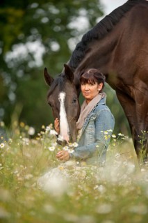 Woman standing beside a Hanoverian horse in a meadow
